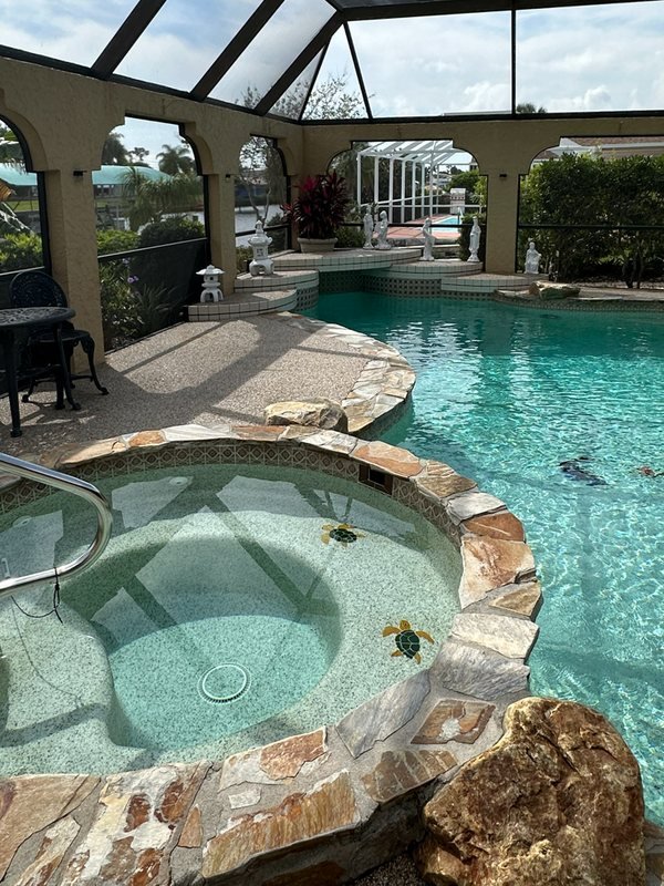 Spa with a natural stone coping beside a river rock pool deck in a screened lanai